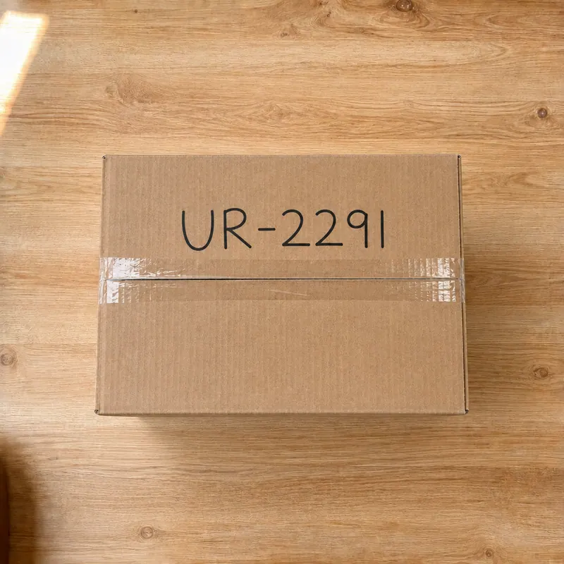 The sealed cardboard box with the code U R dash 2 2 9 1 written on the top by hand.